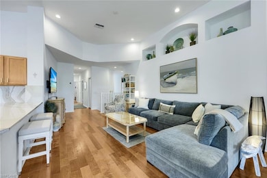 Living room with light wood finished floors, a high ceiling, recessed lighting, and built in shelves