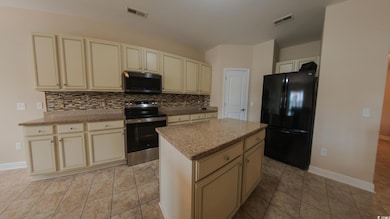 Kitchen featuring stainless steel appliances, cream cabinets, backsplash, a center island, and baseboards