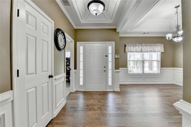Foyer entrance with a chandelier, crown molding, wood finished floors, a wainscoted wall, and a decorative wall