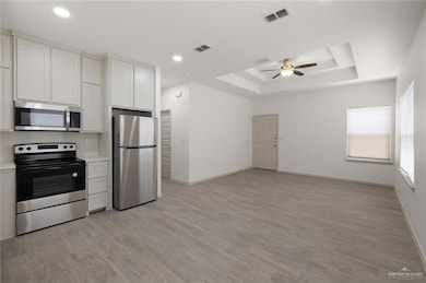 Kitchen featuring appliances with stainless steel finishes, light countertops, a raised ceiling, white cabinets, and recessed lighting