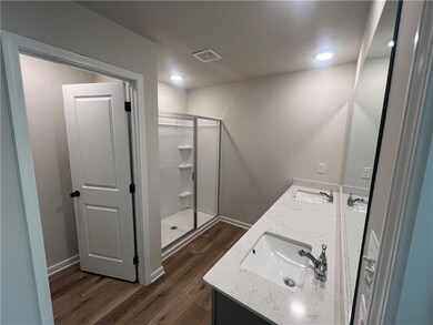 Bathroom with double vanity, wood finished floors, and a stall shower
