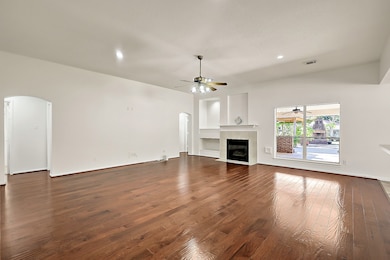 This spacious living room features elegant hardwood floors, a cozy fireplace, and ample natural light from large windows. The open layout is complemented by a ceiling fan and recessed lighting, with easy access to an outdoor patio through glass doors. Ideal for comfortable living and entertaining.