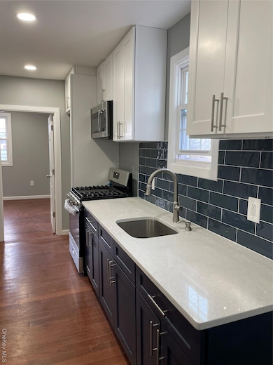 Kitchen with range, light stone countertops, white cabinets, decorative backsplash, and dark wood-type flooring