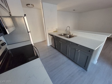 Kitchen featuring a sink, stainless steel appliances, a peninsula, light wood-type flooring, and light stone counters