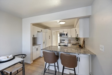 Kitchen with a peninsula, light wood-style flooring, appliances with stainless steel finishes, white cabinets, and a kitchen breakfast bar