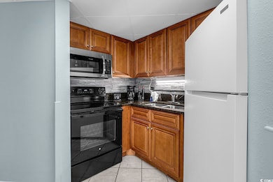 Kitchen with black electric range, freestanding refrigerator, a textured wall, tasteful backsplash, and stainless steel microwave