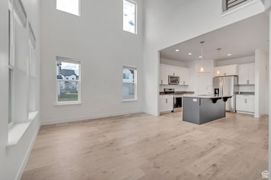 Kitchen featuring a breakfast bar area, stainless steel appliances, plenty of natural light, light wood-type flooring, and a high ceiling