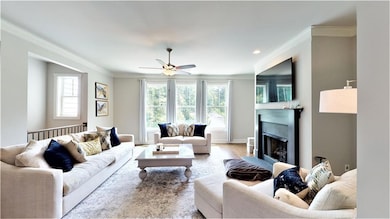 Living area with crown molding, ceiling fan, a fireplace with flush hearth, and wood finished floors