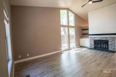 Unfurnished living room with a ceiling fan, wood finished floors, a stone fireplace, high vaulted ceiling, and a textured ceiling