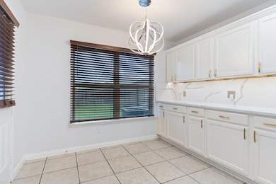 Kitchen with pendant lighting, a notable chandelier, backsplash, light tile floors, and white cabinetry