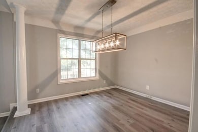 Unfurnished dining area featuring ornate columns, dark wood-style floors, and a chandelier