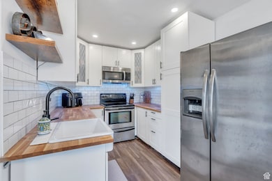 Kitchen featuring wood counters, stainless steel appliances, backsplash, white cabinets, and wood finished floors
