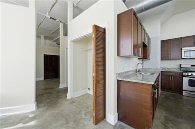 Kitchen featuring concrete floors, stainless steel appliances, light stone counters, and dark brown cabinets