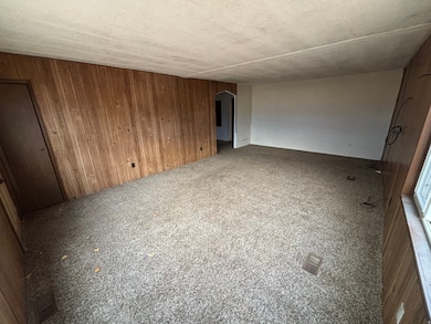 Carpeted spare room with wooden walls, arched walkways, and a textured ceiling