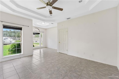 Empty room with a tray ceiling, ceiling fan, and tile patterned floors