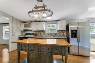 Kitchen with stainless steel refrigerator with ice dispenser, a sink, wood counters, range hood, and a textured ceiling