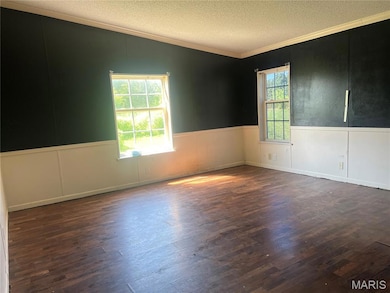 Spare room featuring crown molding, a textured ceiling, a wainscoted wall, and wood finished floors