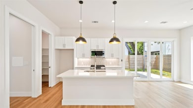 Kitchen with tasteful backsplash, white cabinetry, hanging light fixtures, light wood-style flooring, and recessed lighting
