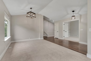 Unfurnished dining area with dark carpet, vaulted ceiling, a chandelier, and dark wood-style flooring