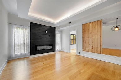 Unfurnished living room featuring a raised ceiling, light wood finished floors, baseboards, and healthy amount of natural light