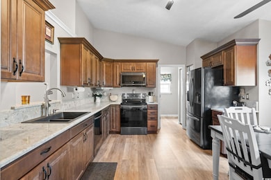 Kitchen featuring stainless steel appliances, lofted ceiling, light wood-style floors, a ceiling fan, and light stone counters