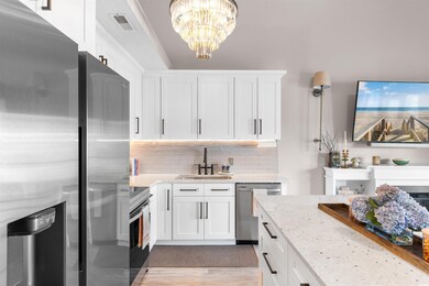 Kitchen with appliances with stainless steel finishes, a sink, white cabinetry, light stone countertops, and backsplash