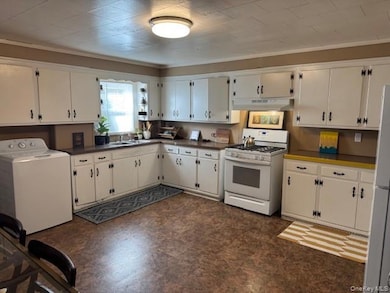 Kitchen with washer / clothes dryer, white appliances, ornamental molding, white cabinetry, and dark countertops