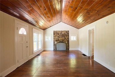 Unfurnished living room featuring wood walls, dark wood finished floors, a fireplace, lofted ceiling, and wood ceiling