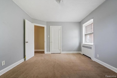 Unfurnished bedroom featuring light colored carpet, radiator, a closet, and a textured ceiling