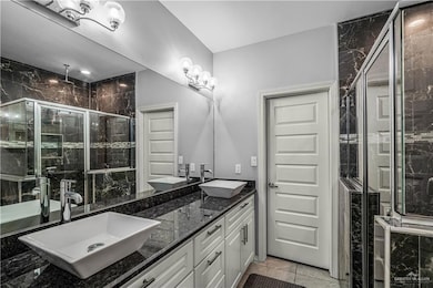 Full bath featuring a marble finish shower, double vanity, and light tile patterned floors