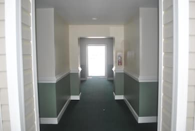 Corridor featuring baseboards and dark carpet