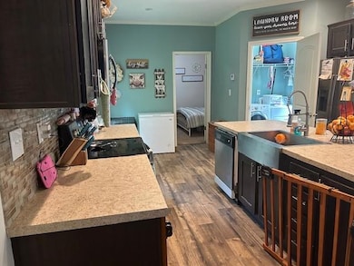 Kitchen featuring dark cabinetry, ornamental molding, stainless steel appliances, dark wood-style floors, and tasteful backsplash