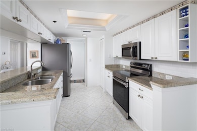 Kitchen featuring appliances with stainless steel finishes, a sink, a raised ceiling, white cabinets, and backsplash