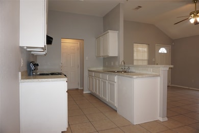 Kitchen featuring a peninsula, white cabinets, light tile patterned floors, a ceiling fan, and vaulted ceiling