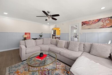 Living area with arched walkways, crown molding, ceiling fan, wood finished floors, and a wainscoted wall