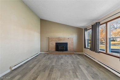 Unfurnished living room with baseboard heating, a baseboard radiator, vaulted ceiling, light wood-style floors, and a textured ceiling