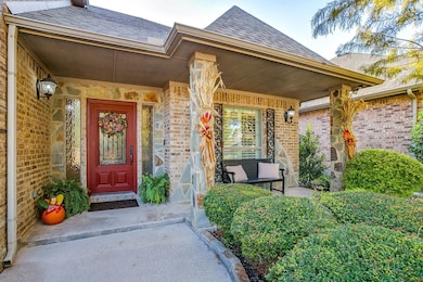 View of exterior entry featuring a porch, a shingled roof, brick siding, and stone siding