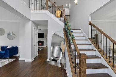 Staircase with wood finished floors, a high ceiling, ornamental molding, and a warm lit fireplace