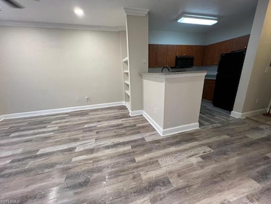 Kitchen featuring black appliances, a peninsula, wood finished floors, light countertops, and ornamental molding