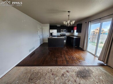 Kitchen featuring appliances with stainless steel finishes, a chandelier, a sink, dark cabinets, and a center island
