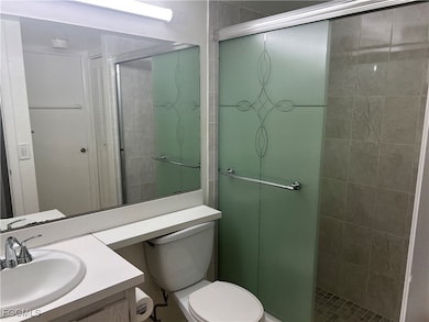 Bathroom featuring an enclosed shower, vanity, and toilet
