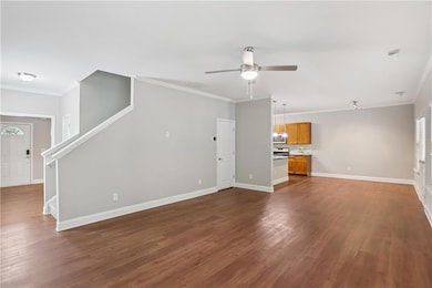 Unfurnished living room with a ceiling fan, dark wood-type flooring, baseboards, ornamental molding, and stairs