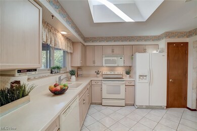 Kitchen featuring light brown cabinets, sink, light tile floors, white appliances, and lofted ceiling with skylight