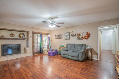 Living room with a textured ceiling, ceiling fan, wood-type flooring, and a brick fireplace