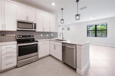 Kitchen featuring stainless steel appliances, a sink, decorative backsplash, a peninsula, and white cabinetry