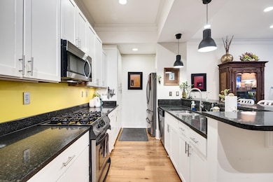 Kitchen with stainless steel appliances, crown molding, a peninsula, light wood-type flooring, and white cabinets