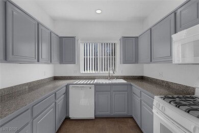 Kitchen with gray cabinetry, white appliances, dark countertops, dark tile patterned flooring, and recessed lighting