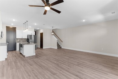 Kitchen featuring open floor plan, hanging light fixtures, tasteful backsplash, a kitchen island with sink, and light wood-style flooring