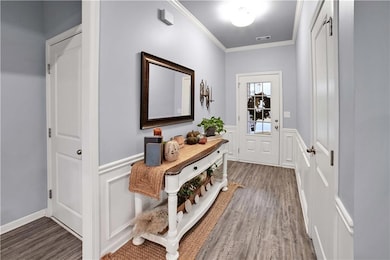 Entryway featuring ornamental molding, a wainscoted wall, a decorative wall, and wood finished floors