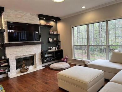 Living room with a stone fireplace, ornamental molding, healthy amount of natural light, and wood finished floors